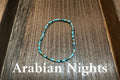 A beaded stretch bracelet made of turquoise blue, black, and gold glass beads, displayed on a dark wood surface.