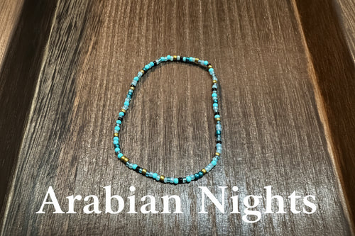 A beaded stretch bracelet made of turquoise blue, black, and gold glass beads, displayed on a dark wood surface.