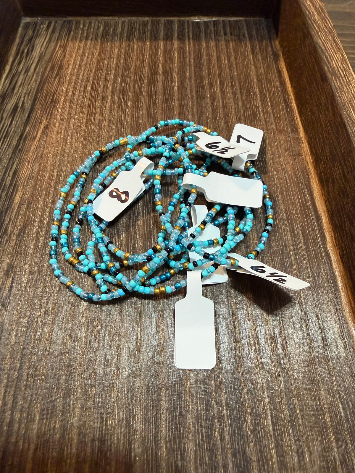 A pile of handmade beaded bracelets in the Arabian Nights color scheme with the size tags on them.
