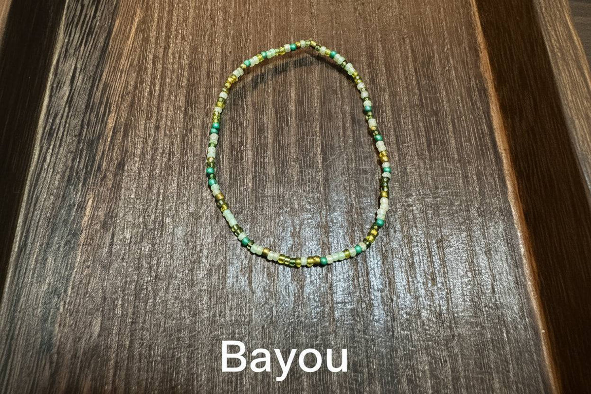 A beaded stretch bracelet made of small green, yellow, gold, and pearl beads, displayed on a dark brown wooden surface.