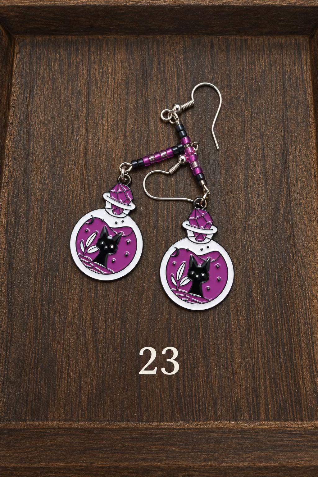 Two silver toned earrings with black, dark fuschia, and light pink beads above purple and light lavender potion bottle charms with cats in the bottles.
