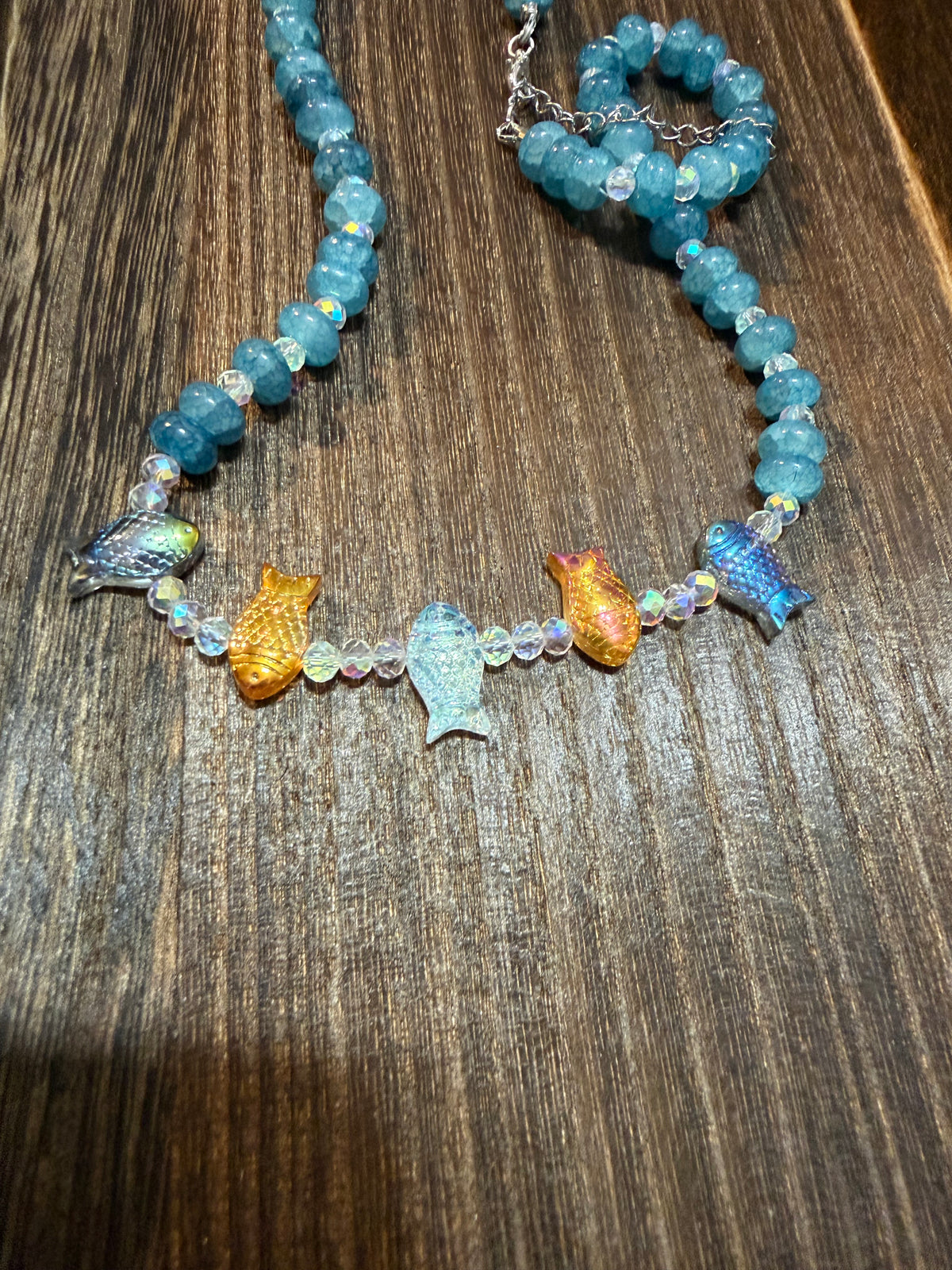 A close up of the aurora borealis glazed glass fish beads as well as the glazed faceted glass beads for bubbles and the natural pattern of the aquamarine stone beads.