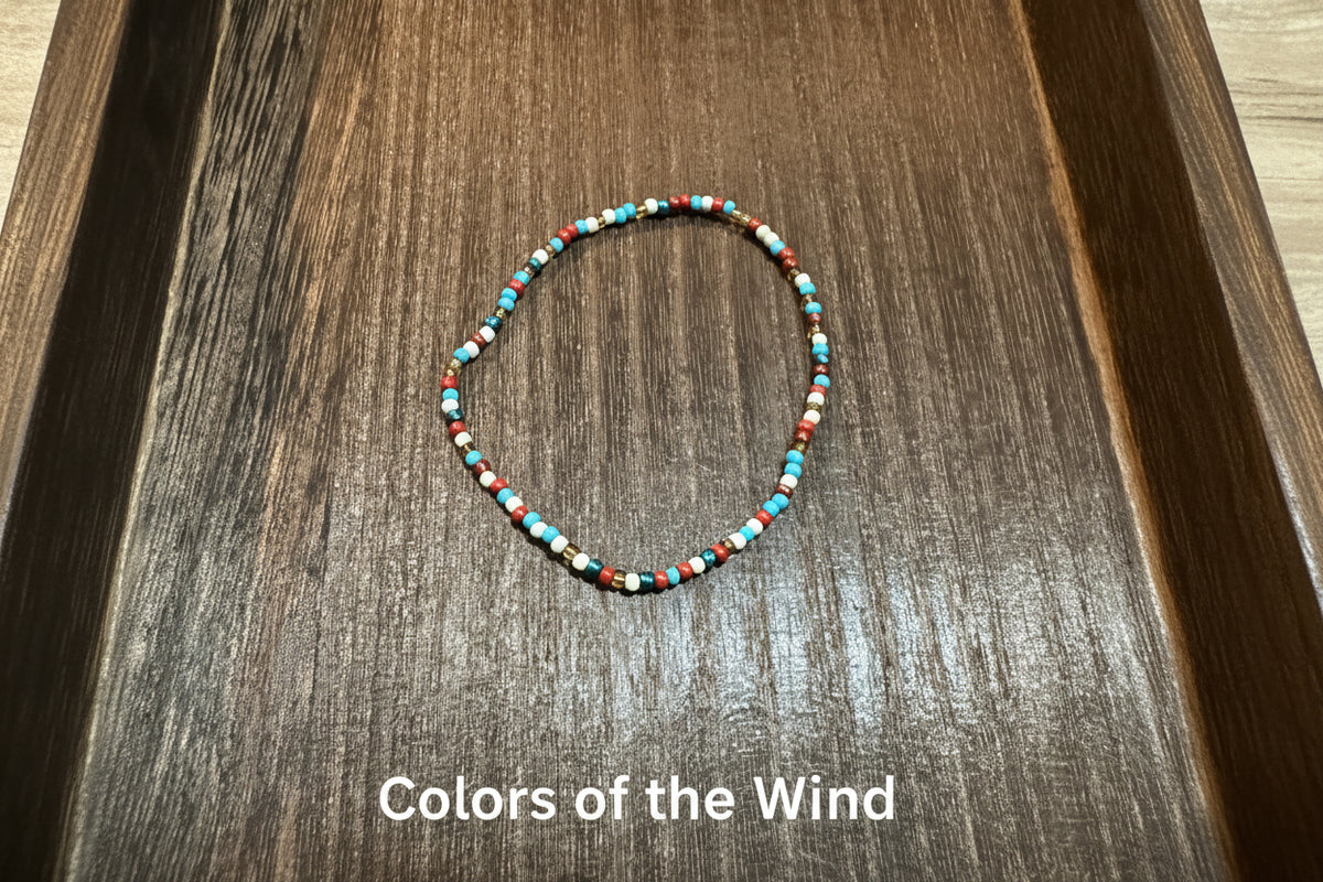 A beaded stretch bracelet with small turquoise, red, white, gold, bronze, and dark brown beads, displayed on a dark wood surface.