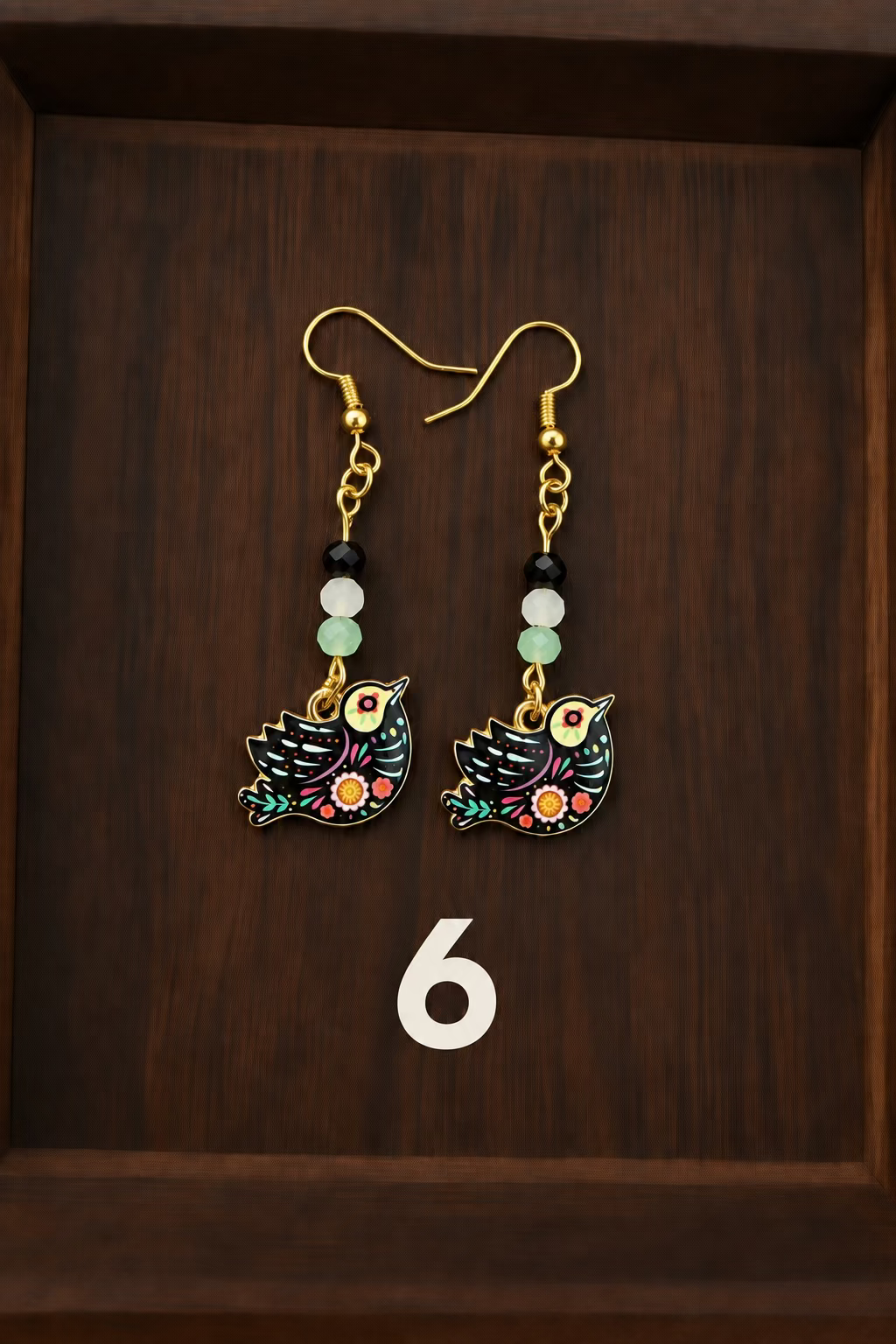 A pair of handmade dangle earrings featuring colorful bird charms and decorative beads, displayed on a dark wooden tray.
