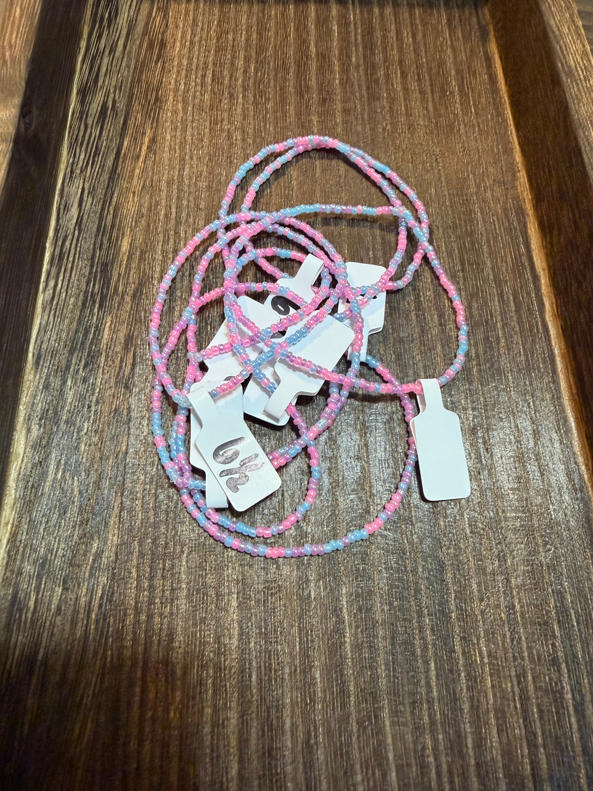A pile of handmade beaded bracelets in the Unicorn color scheme with the size tags on them.