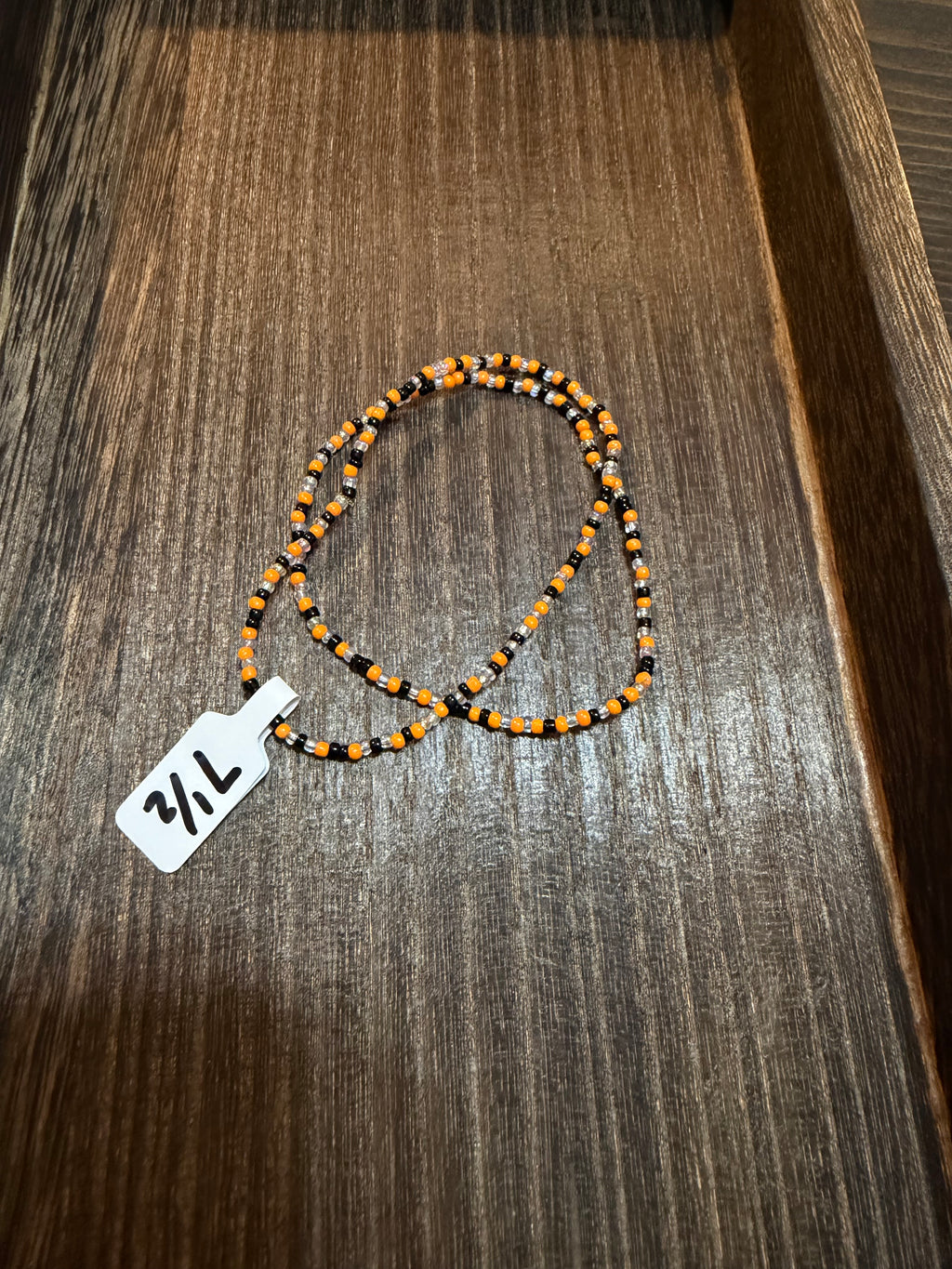A pile of handmade beaded bracelets in the Halloween color scheme with the size tags on them.