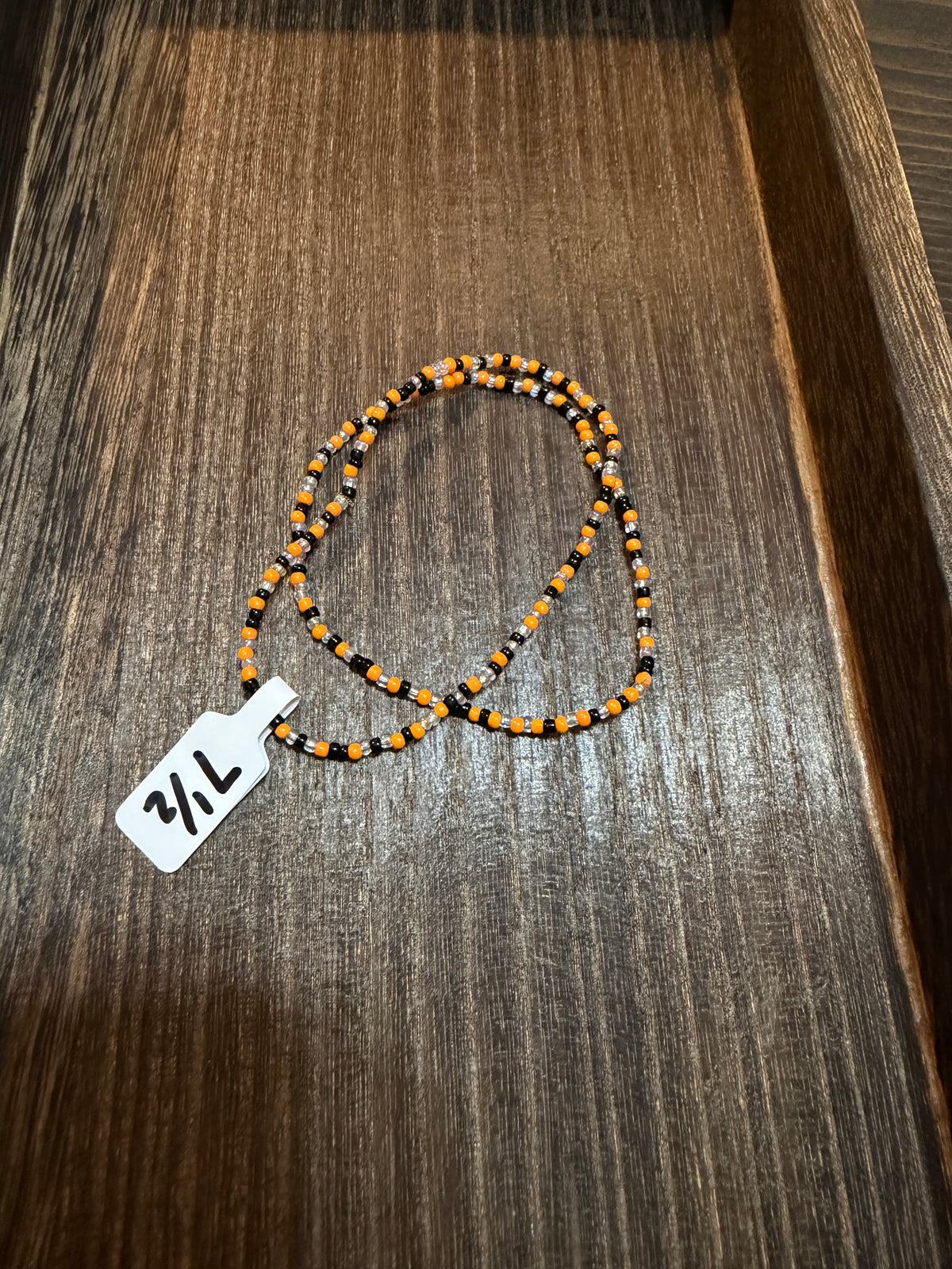 A pile of handmade beaded bracelets in the Halloween color scheme with the size tags on them.