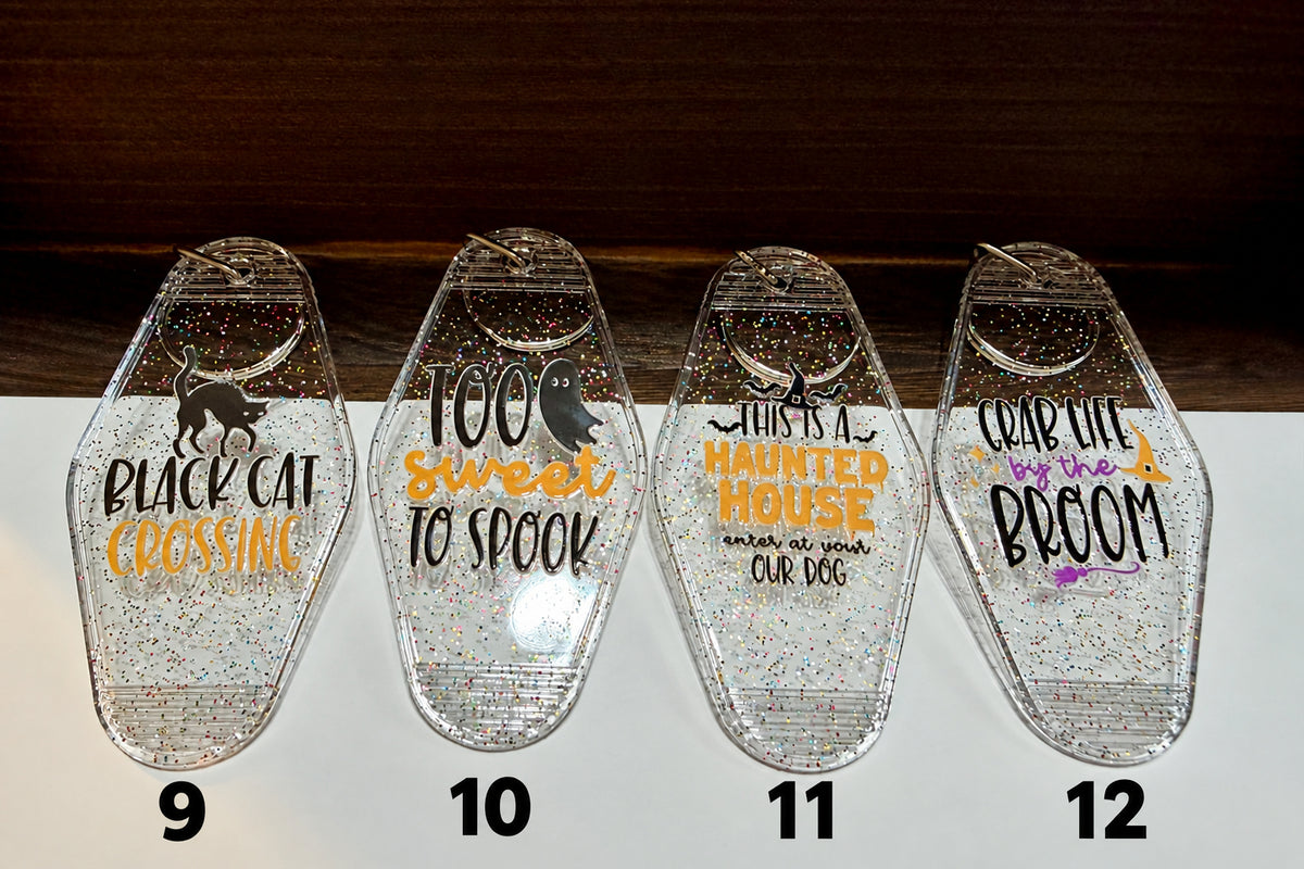 Four coffin-shaped clear resin keepsakes filled with glitter, each printed with a different Halloween-themed phrase and graphic, arranged on a white surface against a dark wood background.