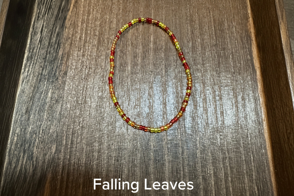 A small beaded loop bracelet made of red, yellow, orange, and light green beads, placed on a dark brown wooden surface.