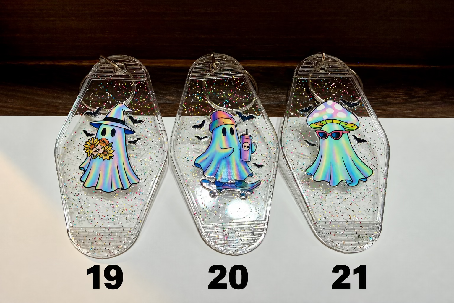 Three clear coffin-shaped glitter keepsakes with colorful ghost illustrations, displayed on a white surface with a dark wood background.