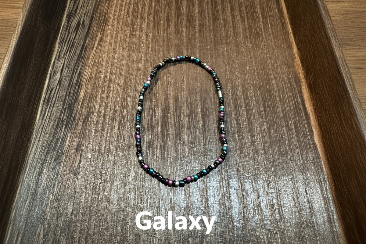 A handmade beaded stretch bracelet made with various shades of black, purple, blue, and silver glass beads.