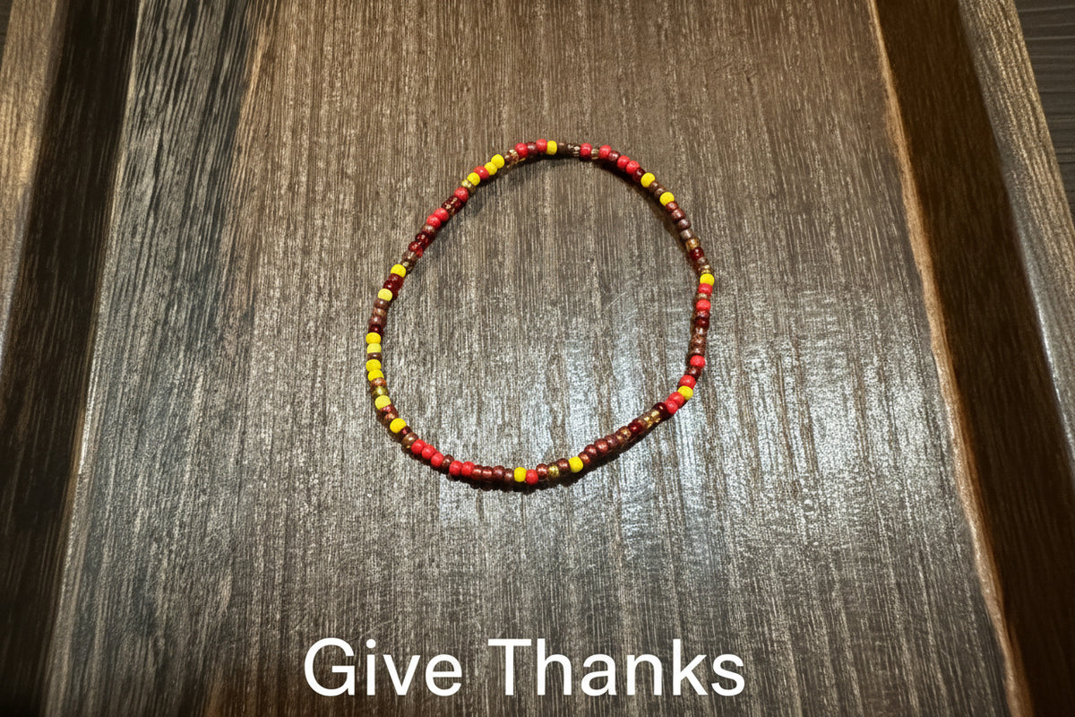 A beaded bracelet made of small red, yellow, gold, and brown beads, arranged in a circle on a dark brown wooden surface.
