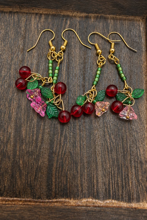 Two pairs of cherry earrings with different colored flower charms and featuring green shimmer beads.