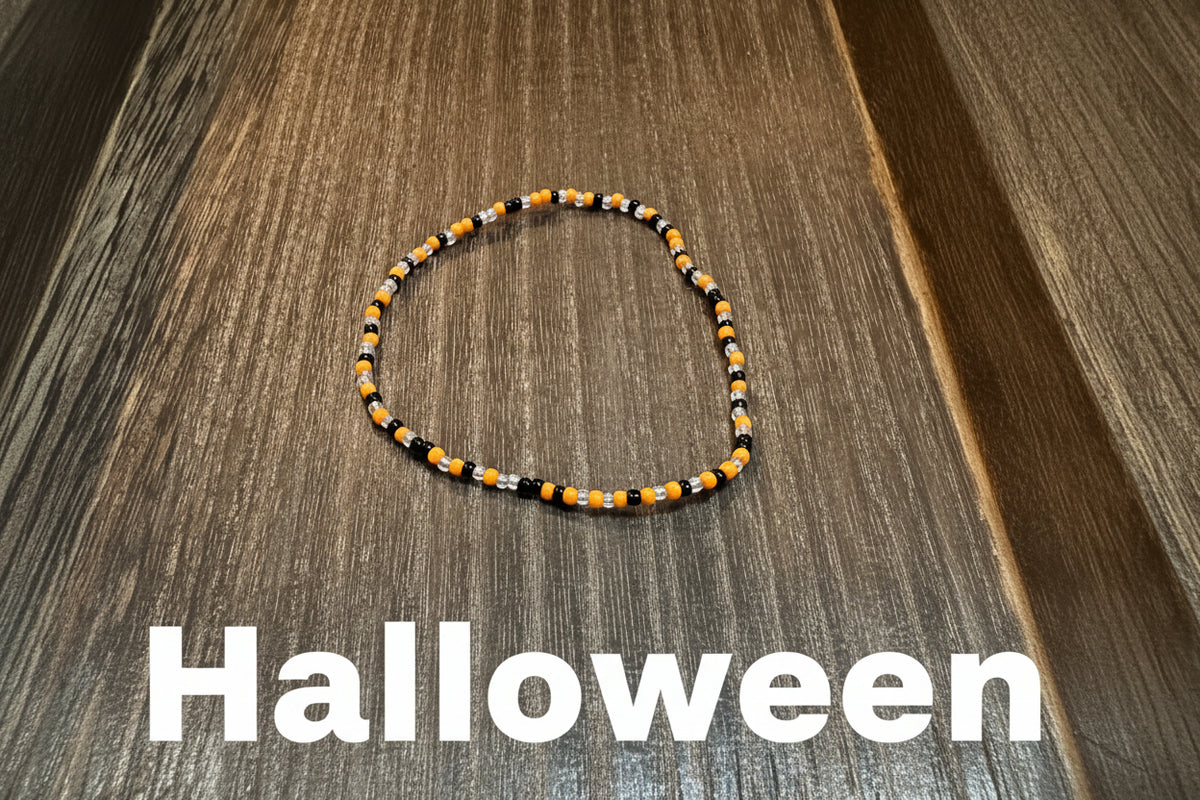 A beaded stretch bracelet with orange, black, and white glass beads, displayed on a dark wood grain surface.