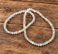 Two beaded bracelets with iridescent, faceted clear beads arranged on a rustic wooden surface.
