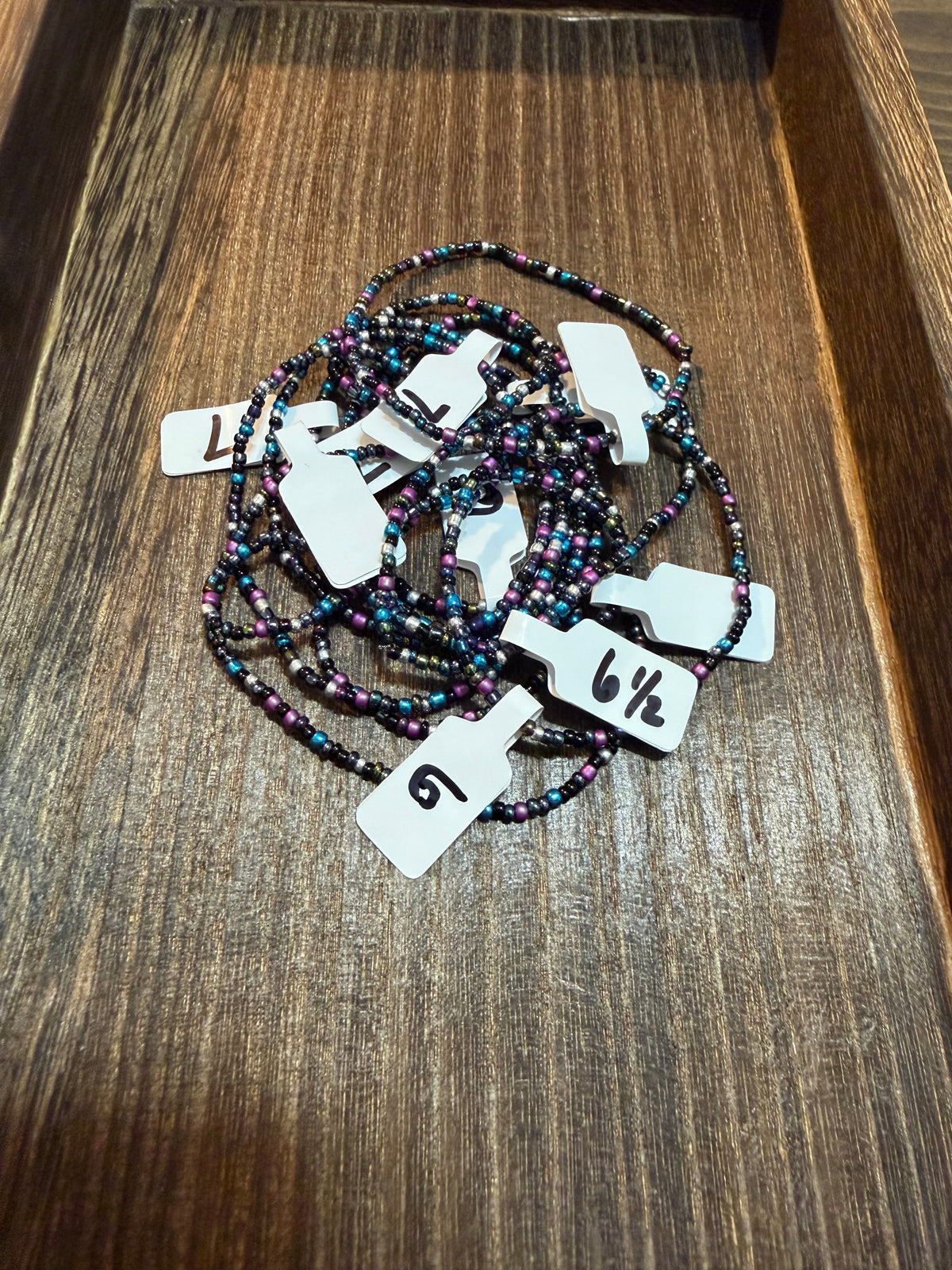 A pile of handmade beaded bracelets in the Galaxy color scheme with the size tags on them.