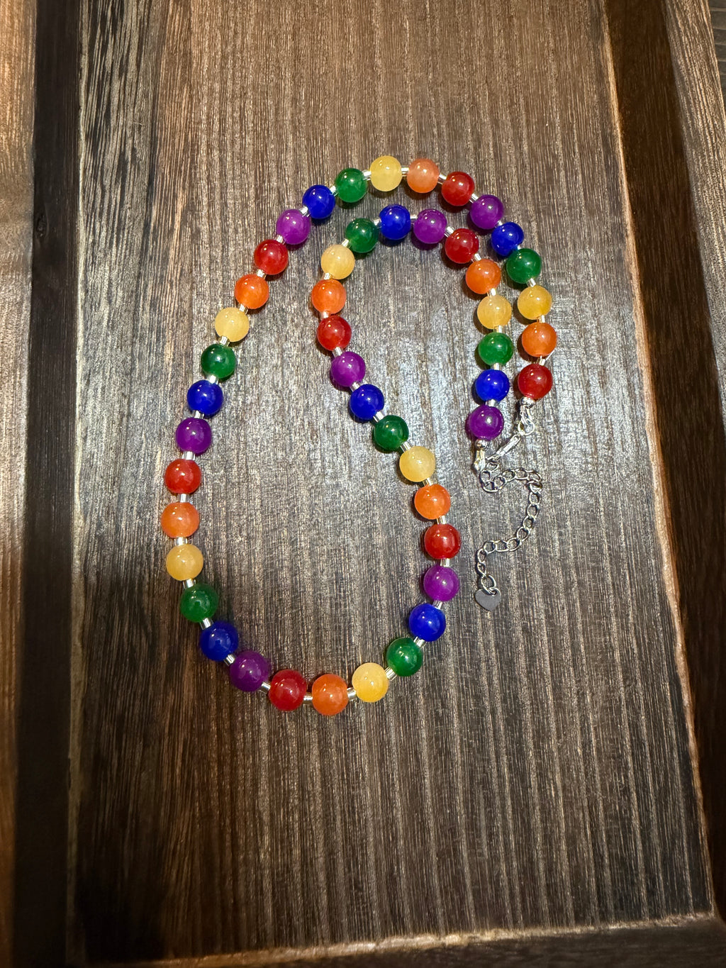 A beaded necklace with colorful round beads in rainbow colors, displayed on a dark wood surface.
