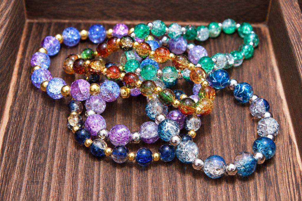 A set of colorful beaded bracelets with metallic gold spacer beads, displayed on a dark wood surface. The bracelets feature a variety of bead patterns and colors including purple, blue, green, orange, and clear glittery beads.