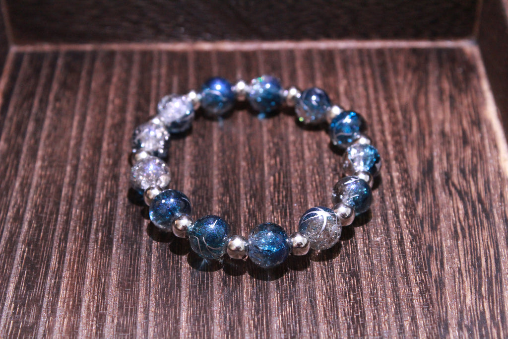A beaded stretch bracelet featuring dark blue crackle beads and small silver spacer beads, displayed on a dark wood surface.