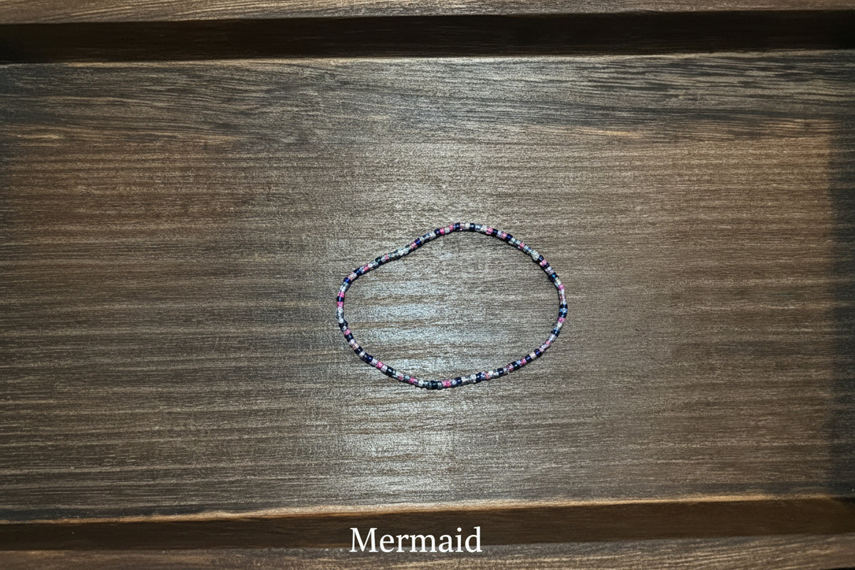 A delicate beaded bracelet with small multicolored beads, resting on a dark brown wooden surface.