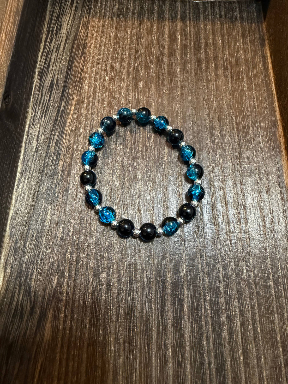 A beaded stretch bracelet featuring black and blue crackle glass beads, displayed on a dark wood surface.