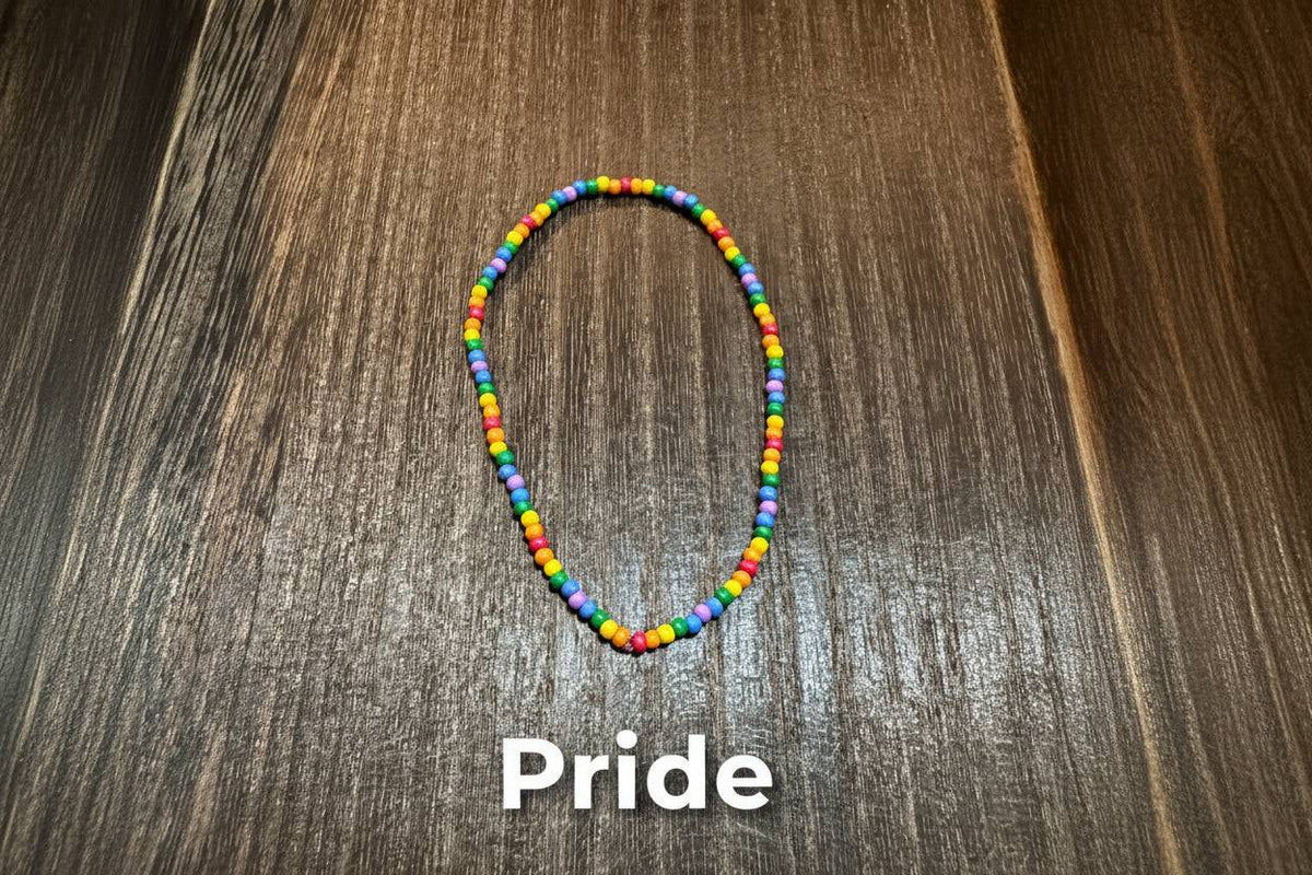 A small beaded bracelet made of colorful round beads in multiple bright colors, placed on a dark brown wood-grain surface.