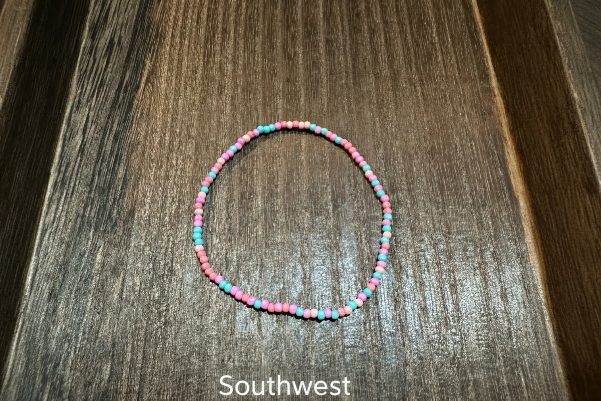 A beaded stretch bracelet made of small pink, coral, and turquoise beads, displayed on a dark brown wooden surface.