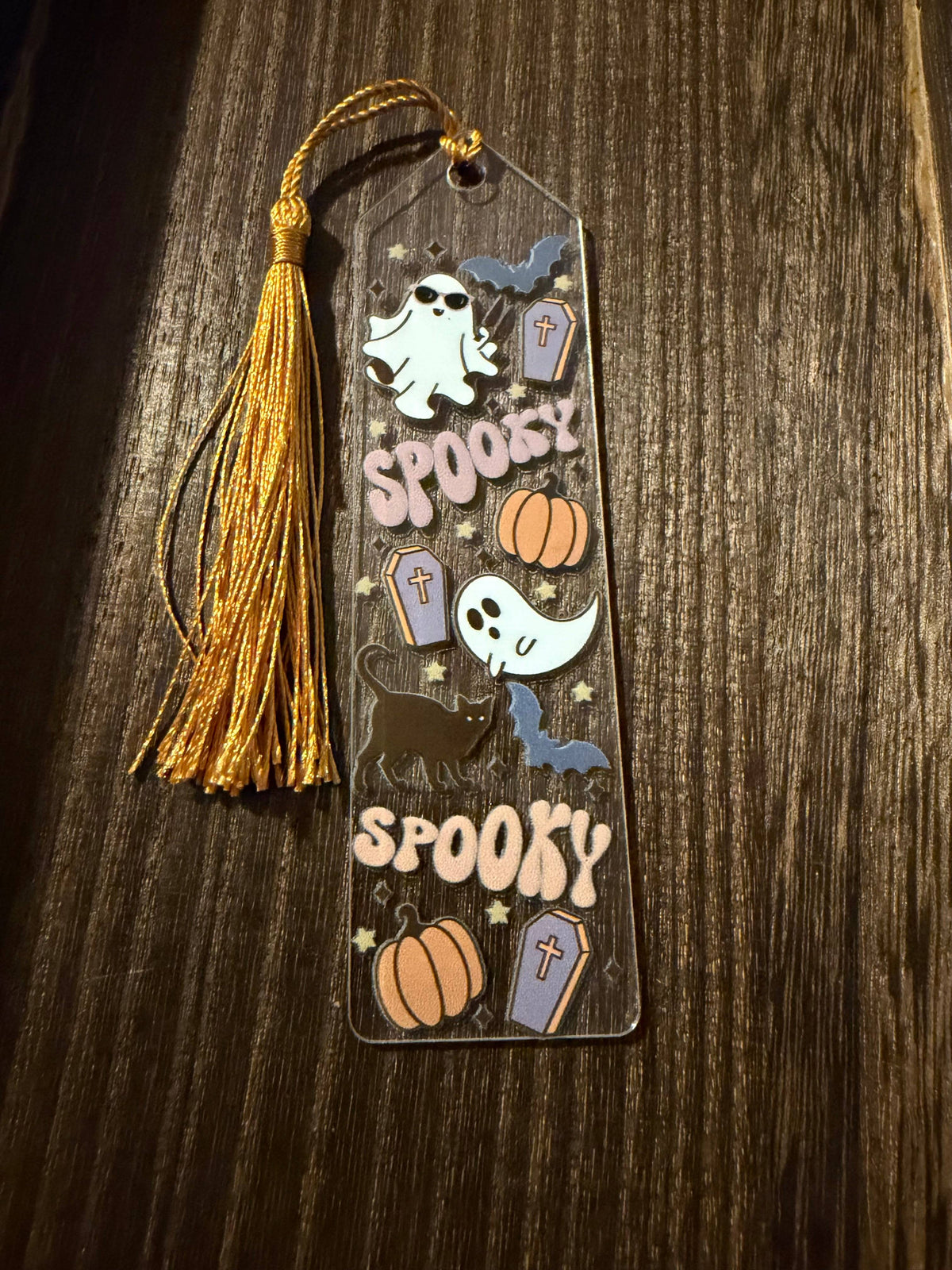 Halloween acrylic bookmark with ghosts, bats, a black cat, tombstones, and pumpkins.  It has a matching gold tassel.