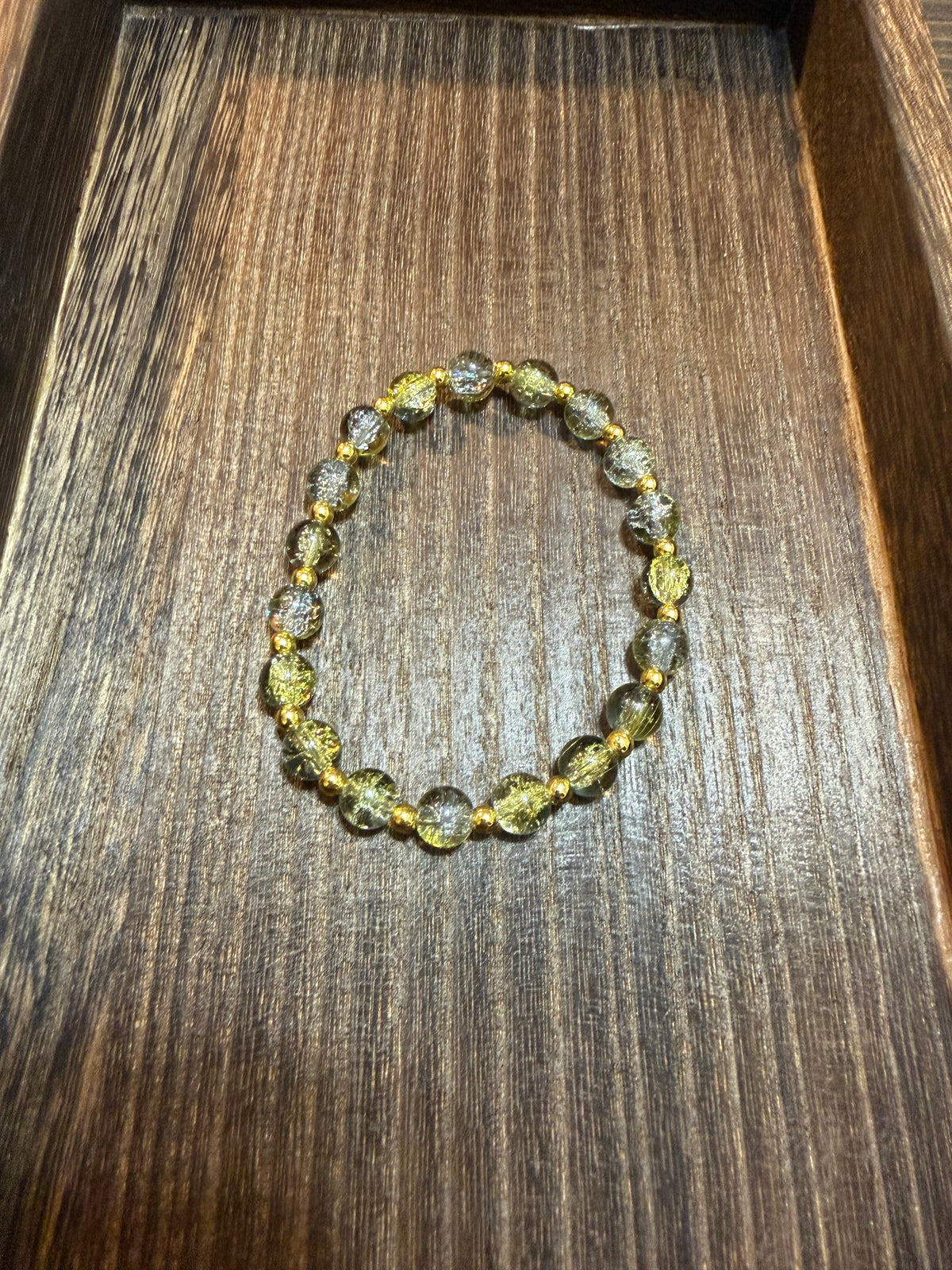A beaded stretch bracelet made of crackle glass gold and silver beads with gold metal accent beads, displayed on a dark brown wooden surface.