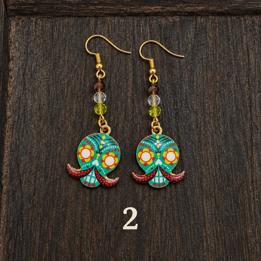 A pair of handmade gold-tone dangle earrings with colorful candy skull charms, displayed on a dark wooden surface.