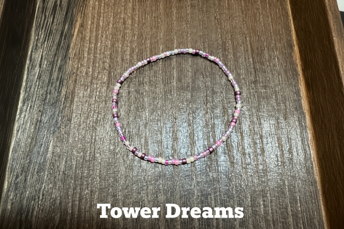 A thin beaded bracelet with pink, purple, lavender, and white beads, arranged in a circle on a dark brown wooden surface.
