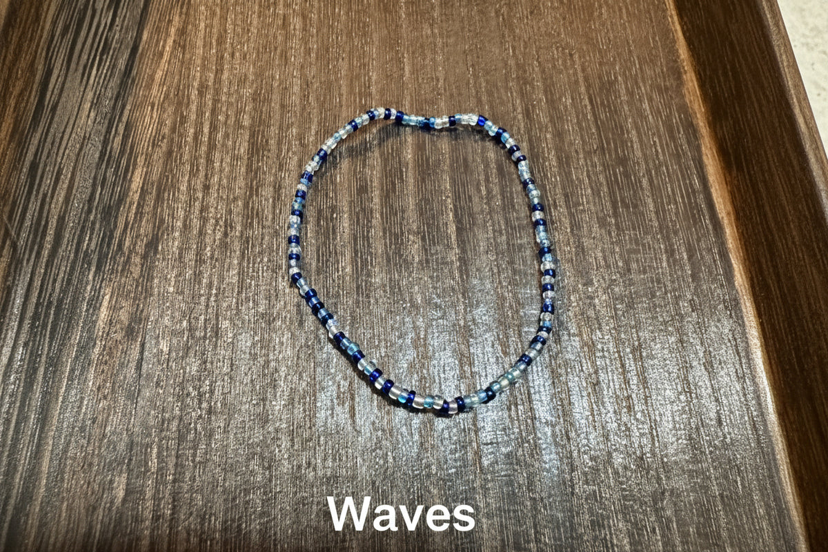 A beaded bracelet made of small blue, white, and navy glass beads, displayed on a dark brown wooden surface.